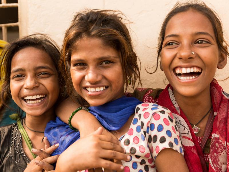 Three Indian teenage girls, laughing with their arms around one another